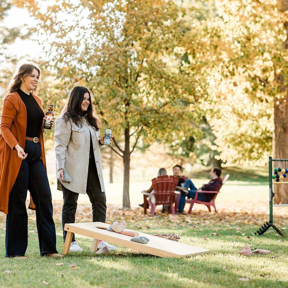 Two women playing cornhole while drinking cider at woodward cider co located at Privato vineyard & winery in Kamloops, BC.