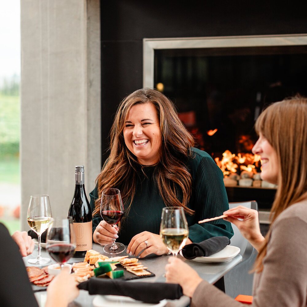 A group of visitors enjoying a bottle of Monte Creek wine with a charcuterie board in front of the fireplace on the patio at Monte Creek Winery near Kamloops, BC.