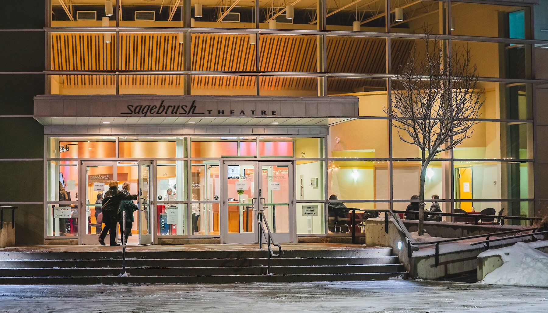 Visitors walking into the warmly light Sagebrush Theatre at night to attend a show in Kamloops, British Columbia.