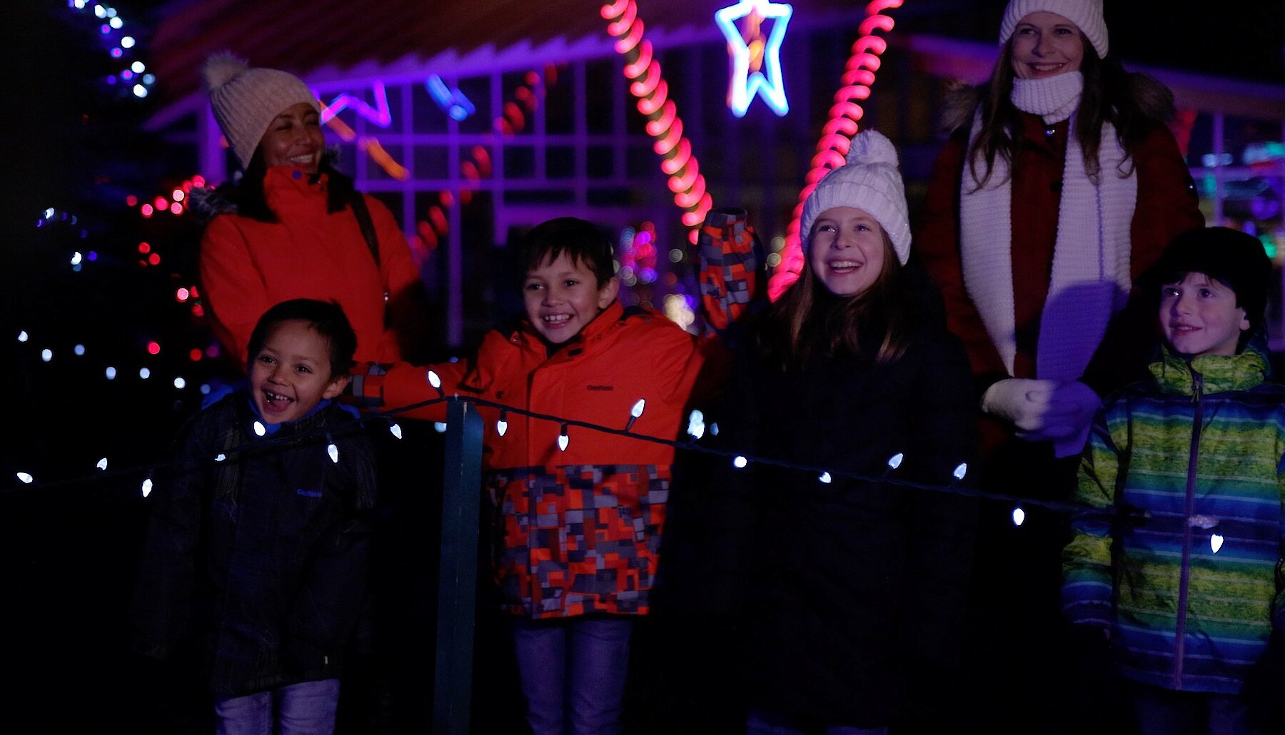 Families dressed in winter gear smiling as they admire the Christmas lights during Wildlights at BC Wildlife Park located near Kamloops, BC.