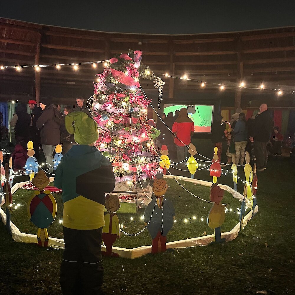 A boy admiring the Who-Ville Kamloops decorated Christmas tree with the Whos gathered around at the Tk̓emlúps te Secwépemc Powwow Arbour.