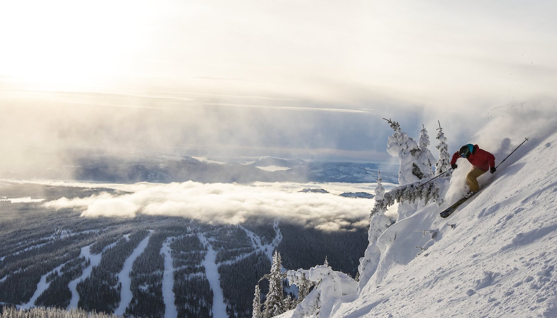 A skier rides down one of the three mountains at Sun Peaks Resort with the rest of the BC mountain resort in the background.