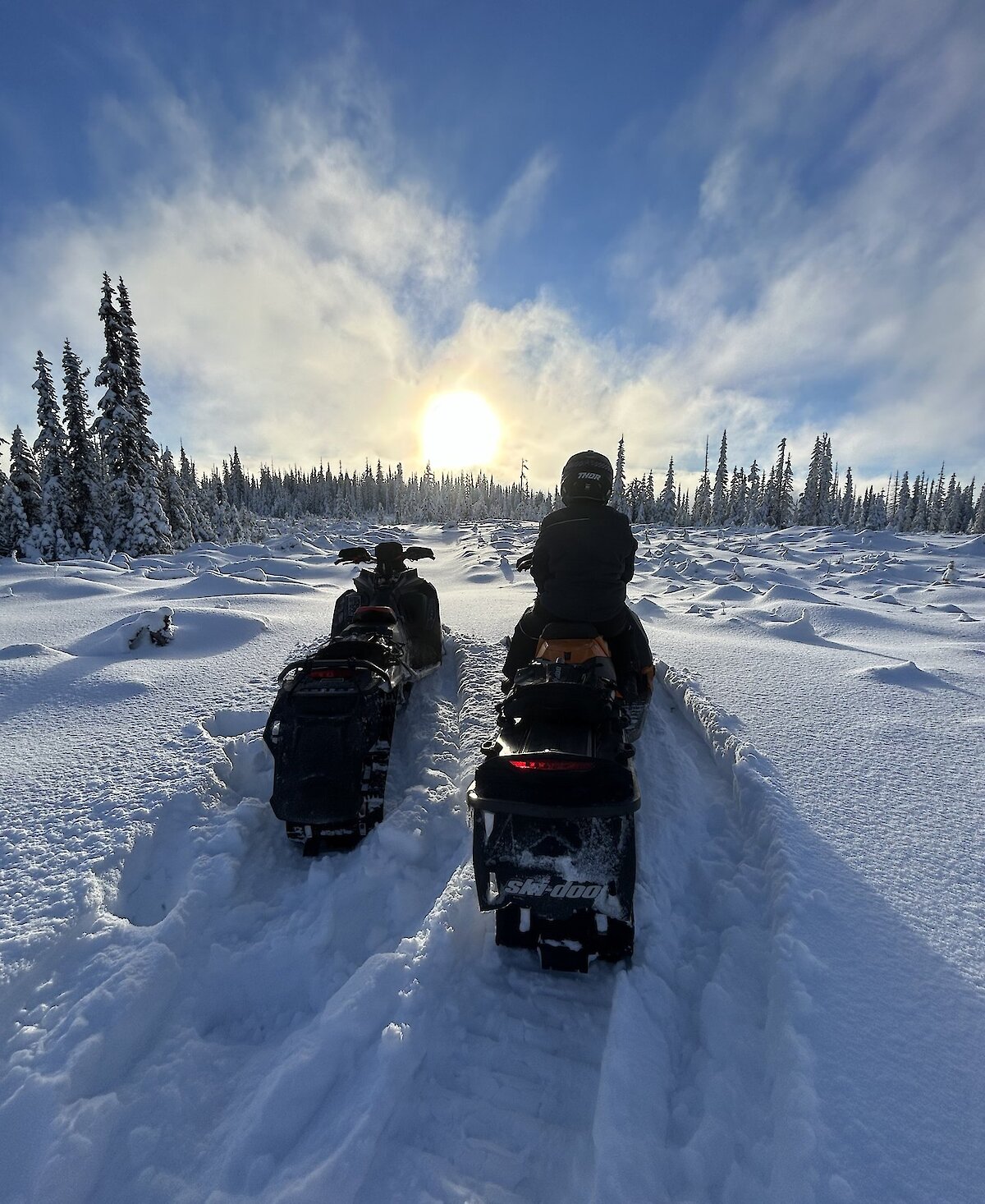 Snowmobiler adminging the winter landscape with deep powder and sunny sky on a tour with Kamloops Snowmobile Adventures.