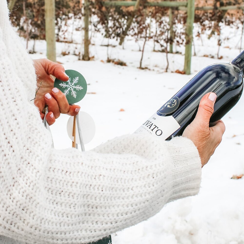 Woman pulling a bottle of Privato wine out of a gift bag with a snowy vineyard in the background at Privato Vineyard and Winery in Kamloops, BC.