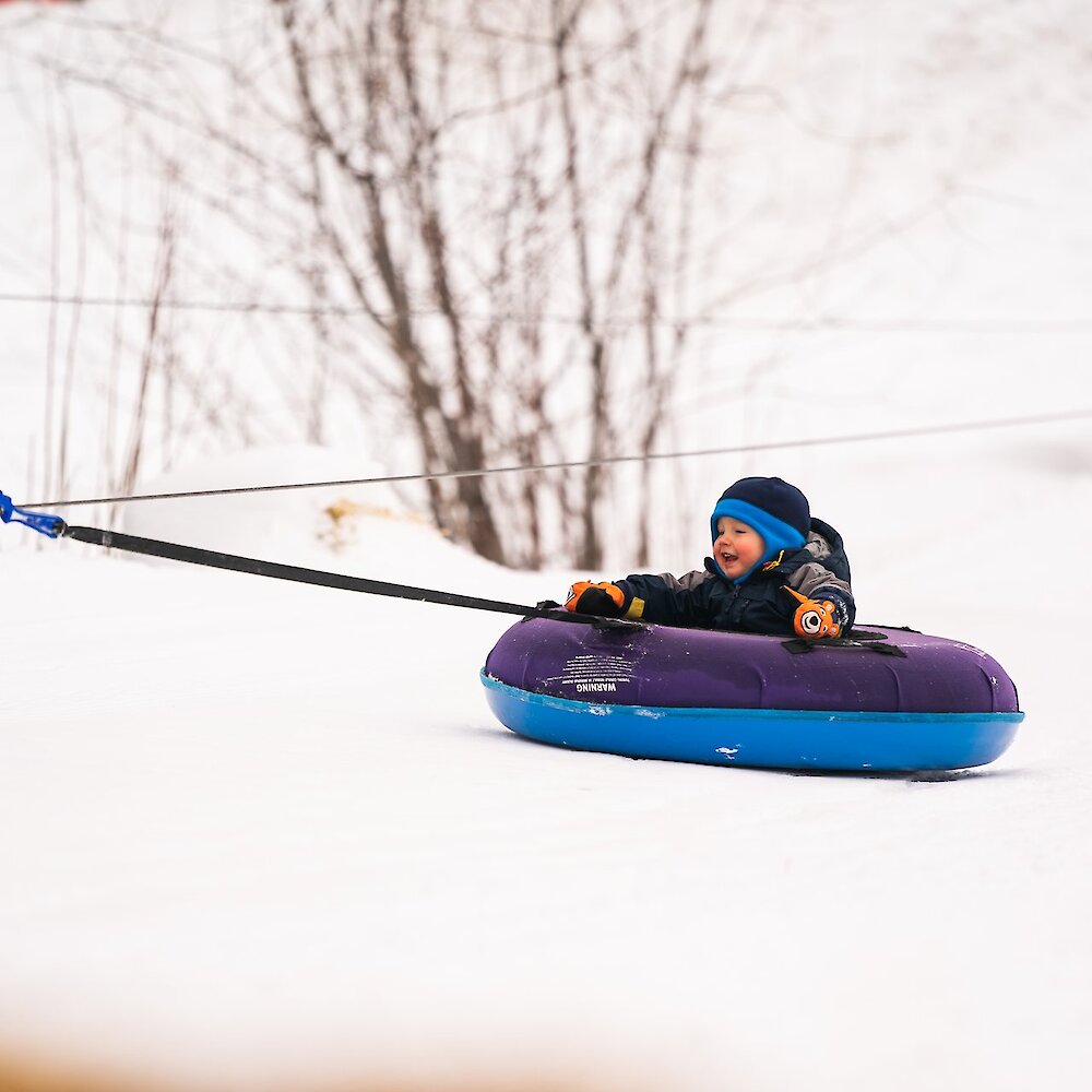 A child smiles while being towed on a tube up a snowy hill at Harper Mountain.