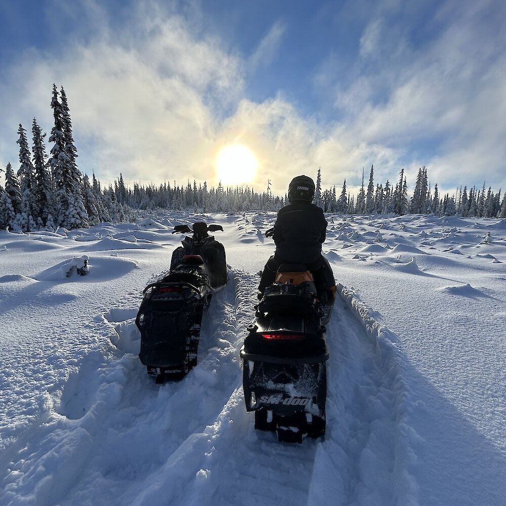 A few sledders on a tour with Kamloops Snowmobile Adventures taking a break and admiring the sun over the snowy landscape, near Kamloops, BC.