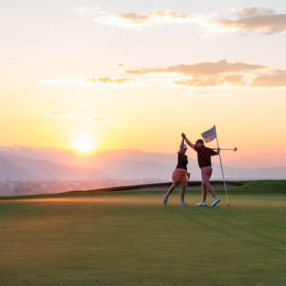 A couple hit fives on the golf course at Bighorn Golf & Country Club with the sunset in the background.