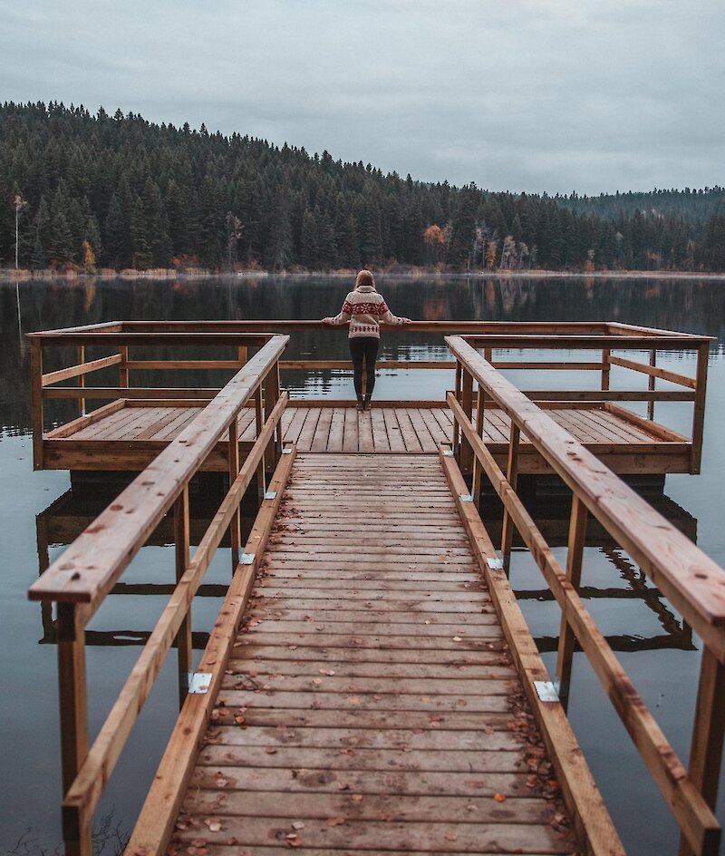 A woman on a dock at Isobel Lake admiring the fall foliage around the shoreline in Kamloops, BC.