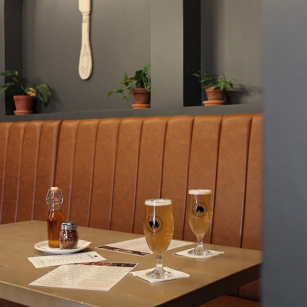 A booth table is set with menus and two glasses of beer.