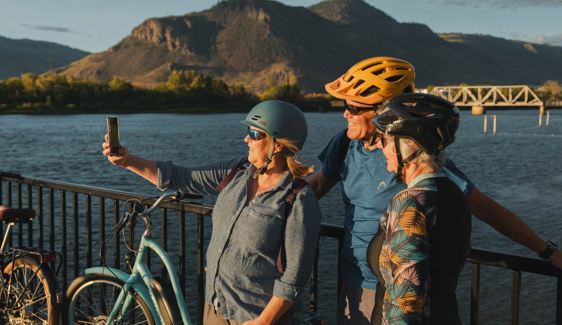 A group of three cyclists take a selfie in front of a river.