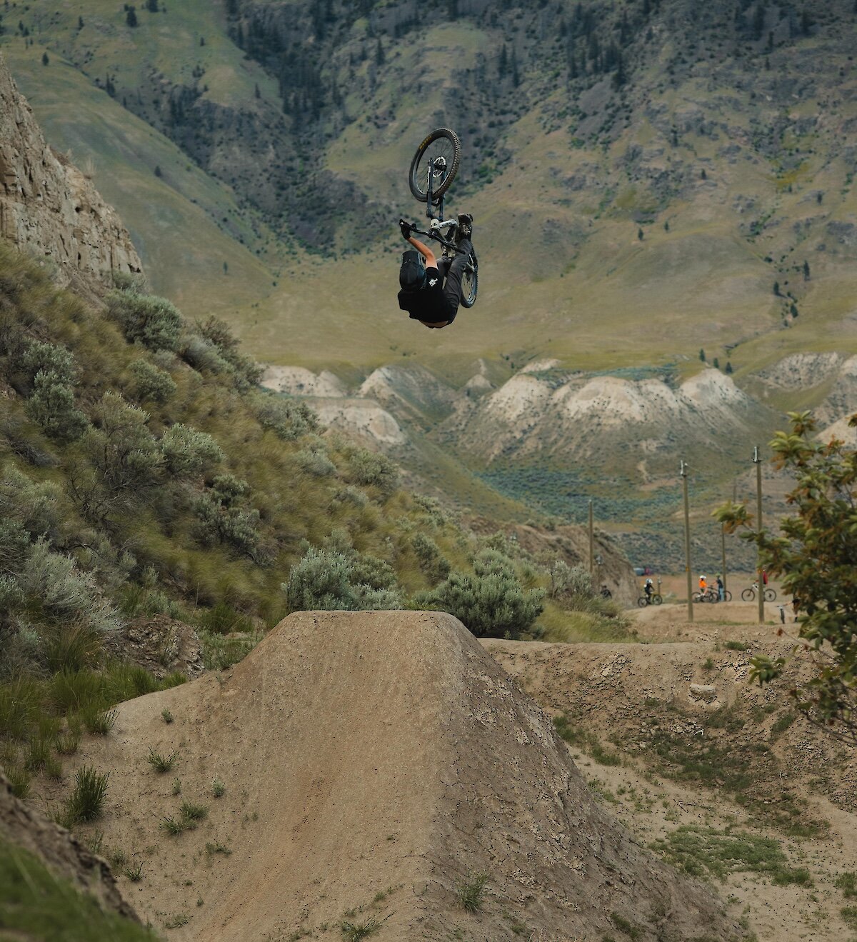 Mountain biker performing a jump with the mountains in the background at the Kamloops Bike Ranch.