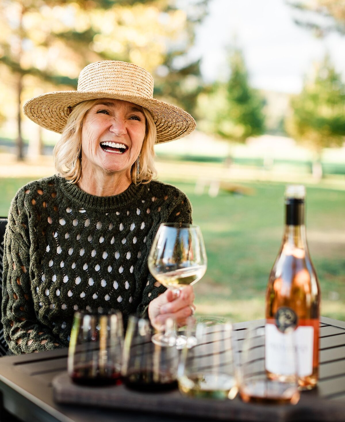 A woman smiling with her glass of wine on the patio at Privato Vineyard and Winery in Kamloops.