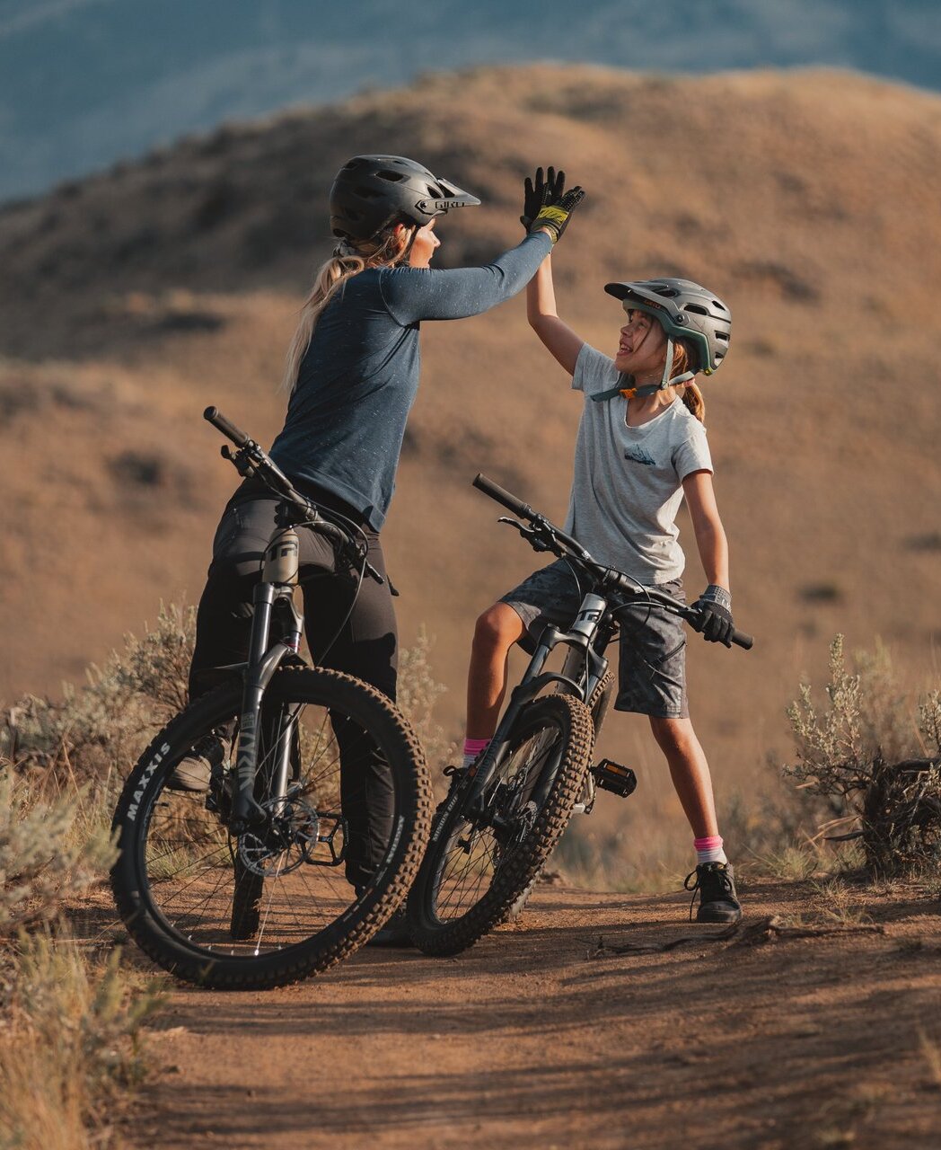 A mom and daughter high five while mountain biking in Lac du Bois grasslands in Kamloops, BC.
