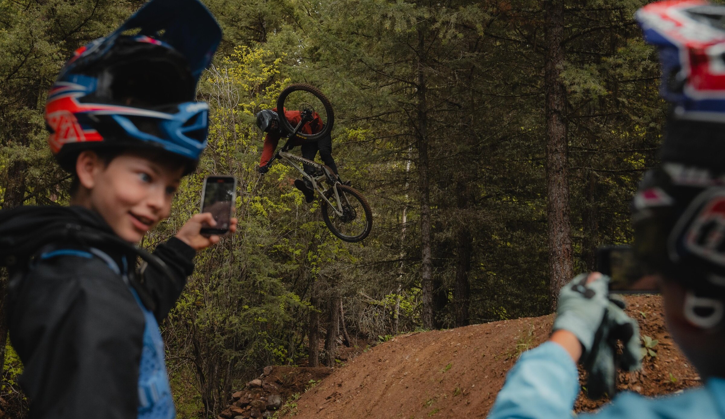A mountain biker taking a photo while another biker gets air off a jump at Harper Mountain, near Kamloops, BC.